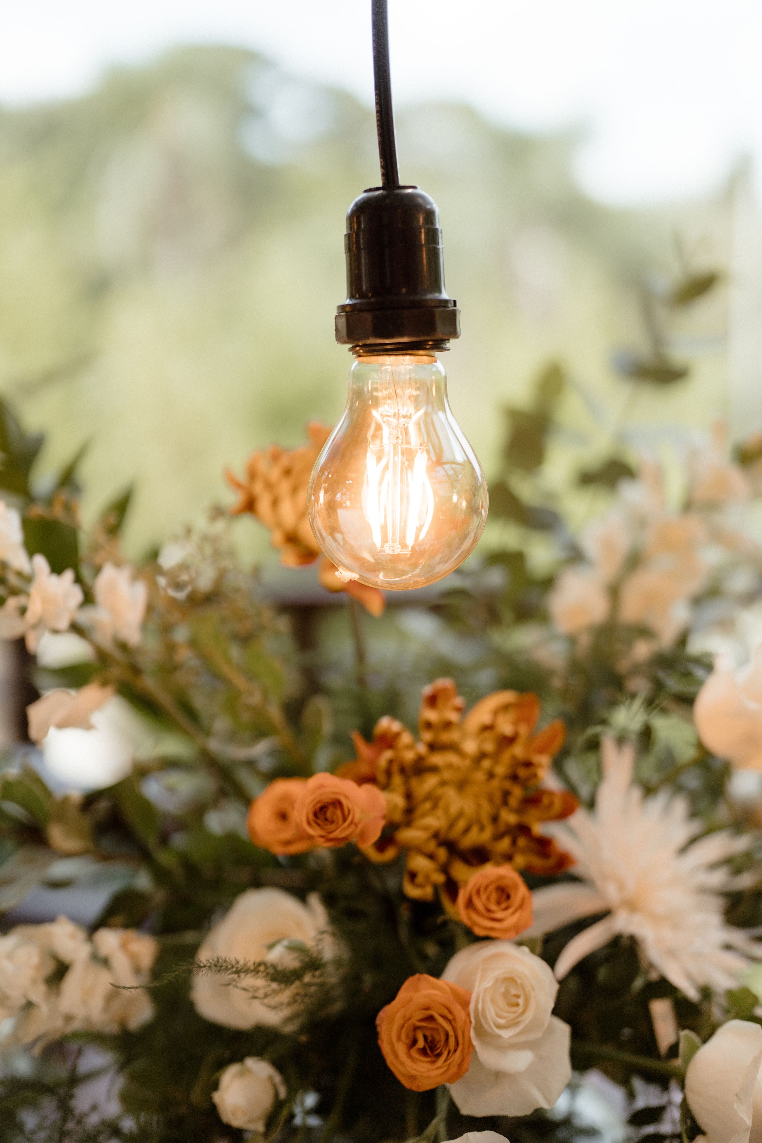 Vintage Edison bulb hanging over peach and cream floral arrangements.