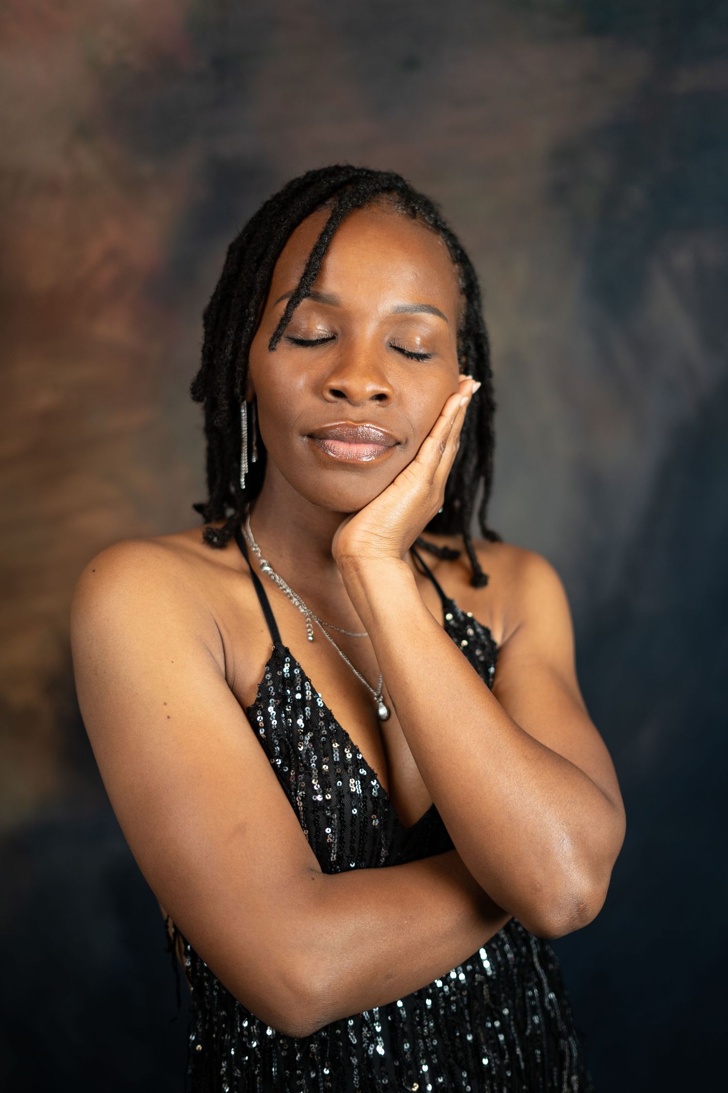 Serene portrait with gentle pose in sequined black dress against dramatic backdrop.