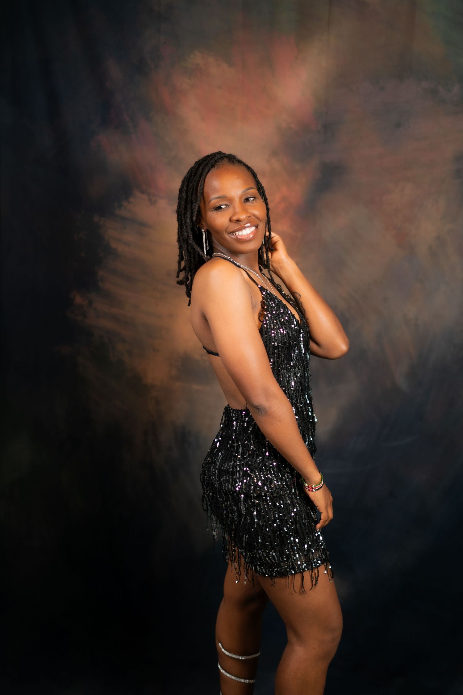 Portrait of model in black sequined cocktail dress against moody backdrop.