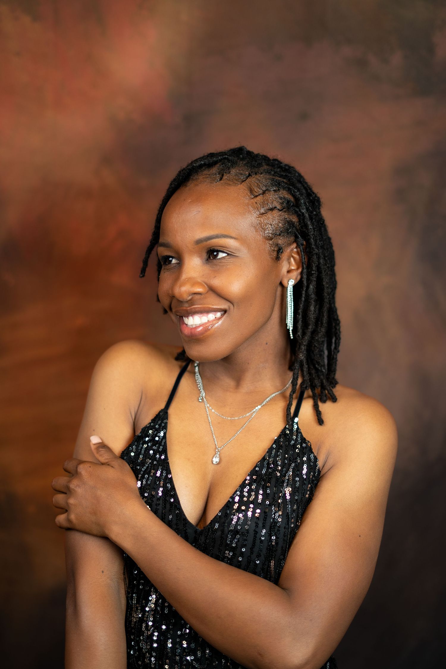 Studio portrait showing elegant pose in sparkly black dress with statement jewelry.