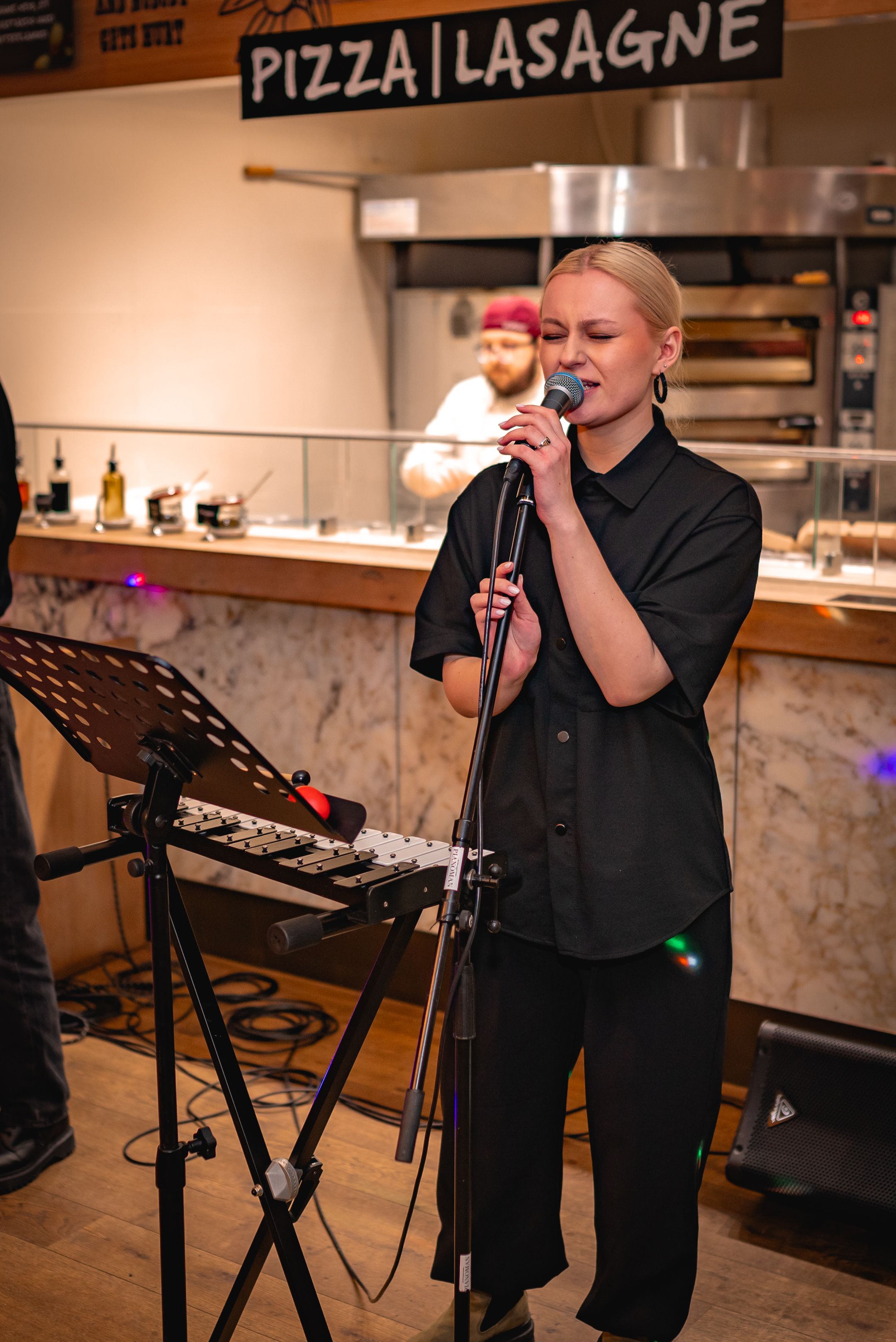 Live musical performance at a restaurant with pizza and lasagne menu sign visible.