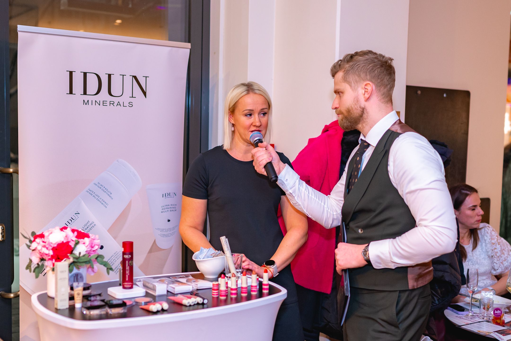 Beauty product demonstration at IDUN Minerals booth with display table and banner.