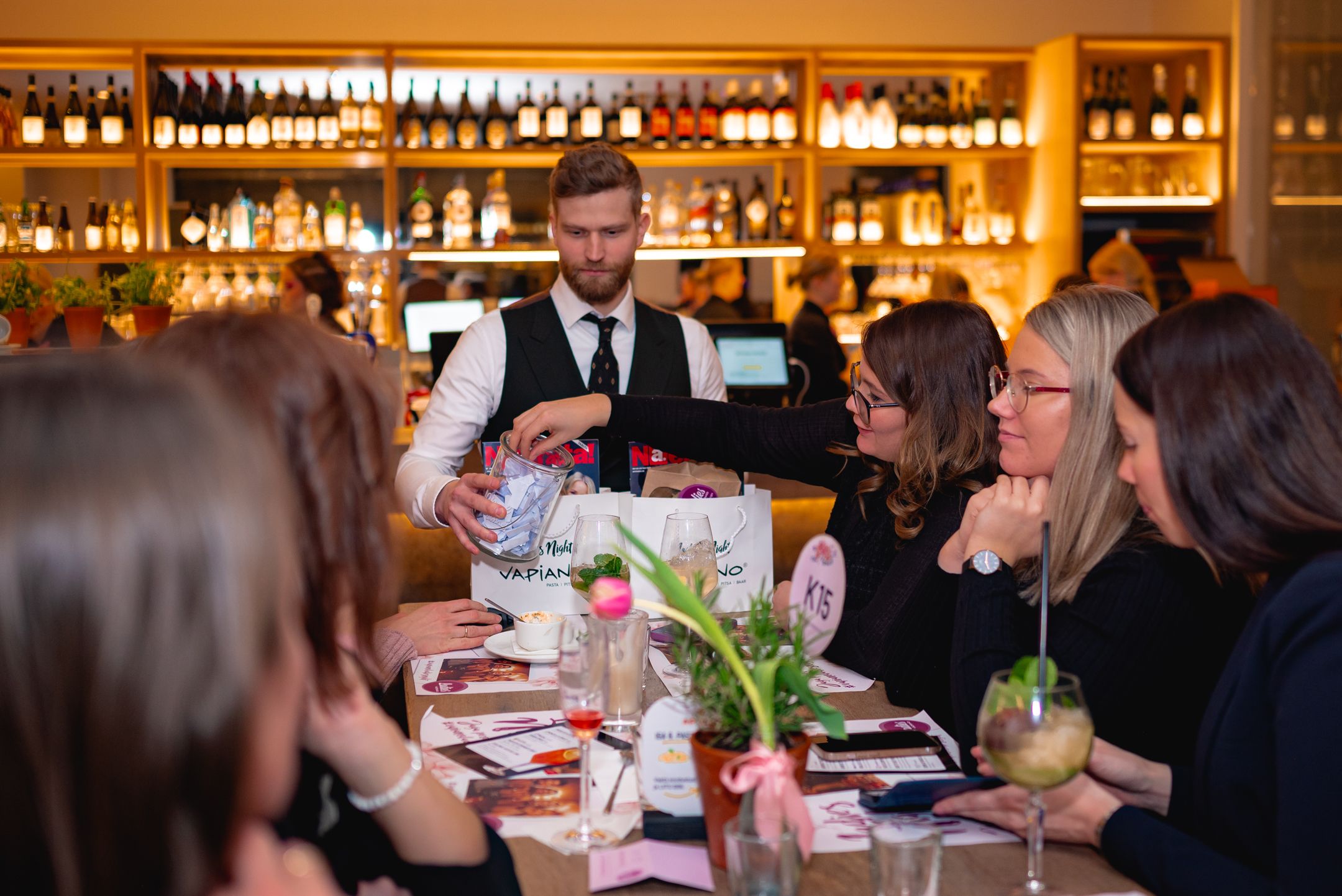 Server in formal attire taking orders from guests at an upscale restaurant bar.