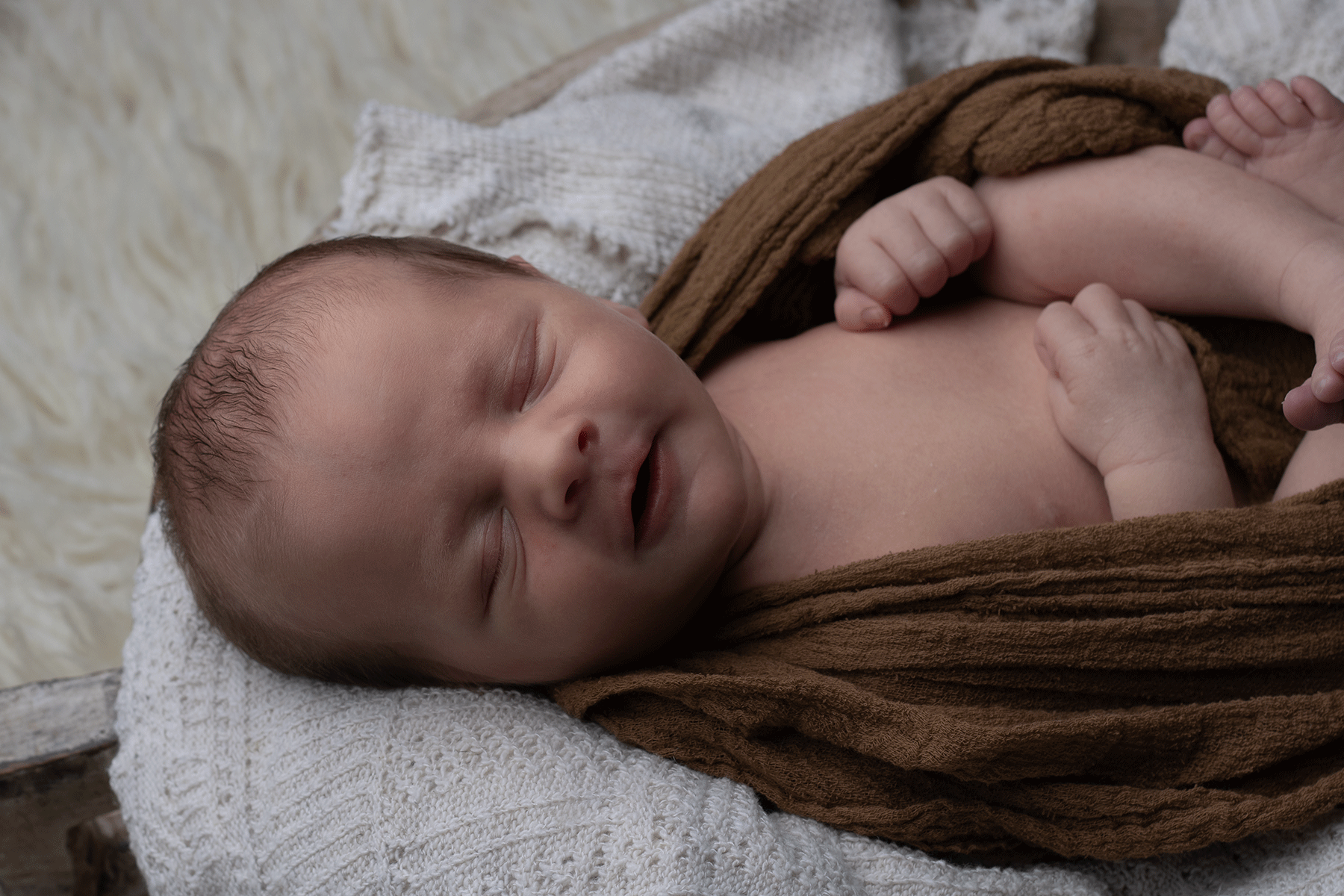 Newborn boy wrapped in a brown cheesecloth, in a wooden prop, during a newborn session with Ceris Hicks Photography