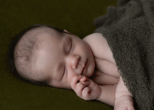Sleeping newborn, wrapped in a green wrap, on a green blanket during a newborn session in Ceredigion