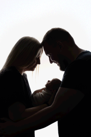 Backlit family photograph, including mum, dad and baby, taken during an in-home Newborn session in Wales
