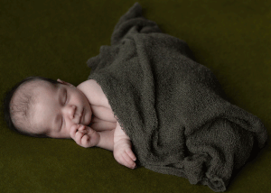 Newborn baby boy asleep on a dark green blanket during a session with West Wales newborn photographer