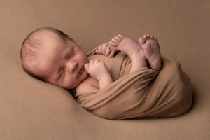 Newborn baby boy wrapped in a soft brown blanket, sleeping peacefully on a brown backdrop during a Ceredigion newborn session