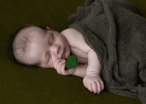 Newborn holding a green heart, sleeping on a green background during newborn session with Ceris Hicks Photography
