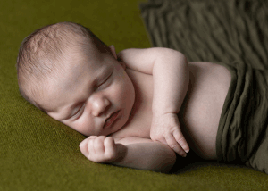 Newborn wrapped in green fabric, sleeping peacefully on their side during session with professional newborn photographer in Ceredigion
