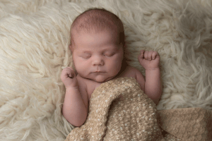 Newborn sleeping with arms up on a cream flokati during a newborn session in Ceredigion
