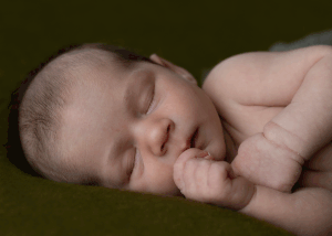 Newborn sleeping peacefully on a green background during a newborn session in West Wales