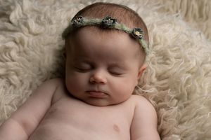 Baby girl wearing green floral headband, while sleeping peacefully on a cream flokati captured by Ceris Hicks Photography