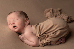 Newborn draped in a brown fabric, sleeping on a brown background during an in-home Ceredigion Newborn Session