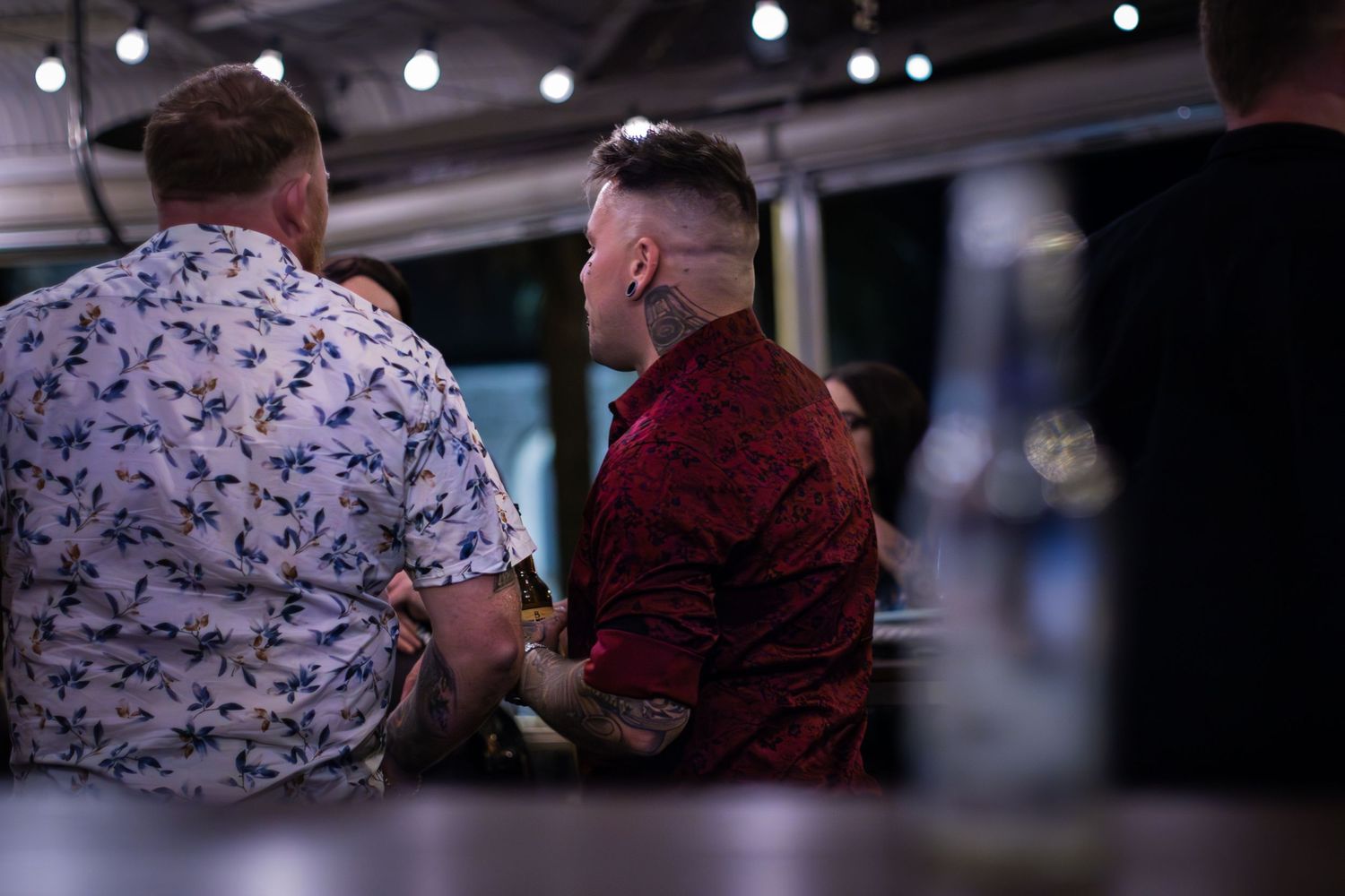 Two people sitting together at a bar with string lights in the background.