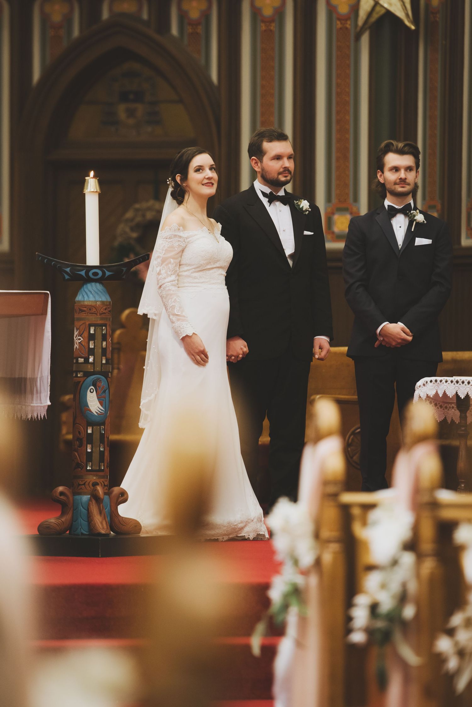 a bride and groom stand on the alter looking at the parishioners at st andrew's cathedral in victoria british columbia.