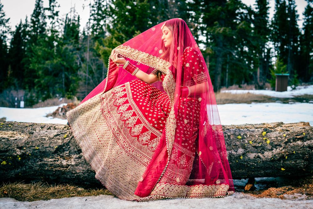 Red and gold embellished lehenga dress displayed against snowy winter landscape.