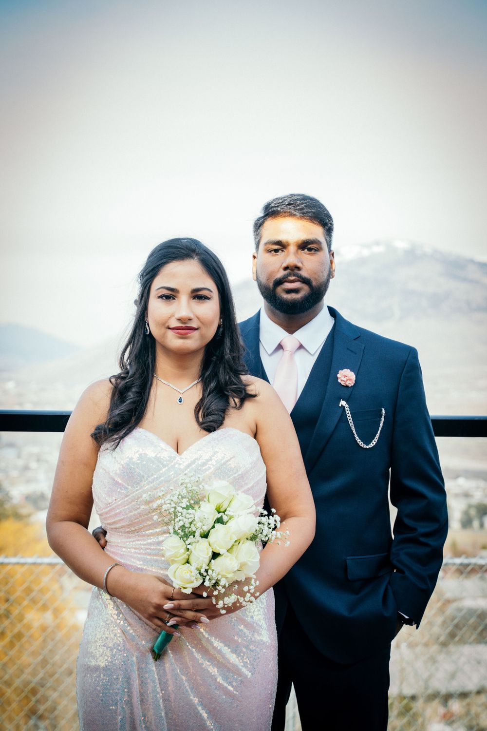 Wedding couple in formal attire posing against mountain backdrop.