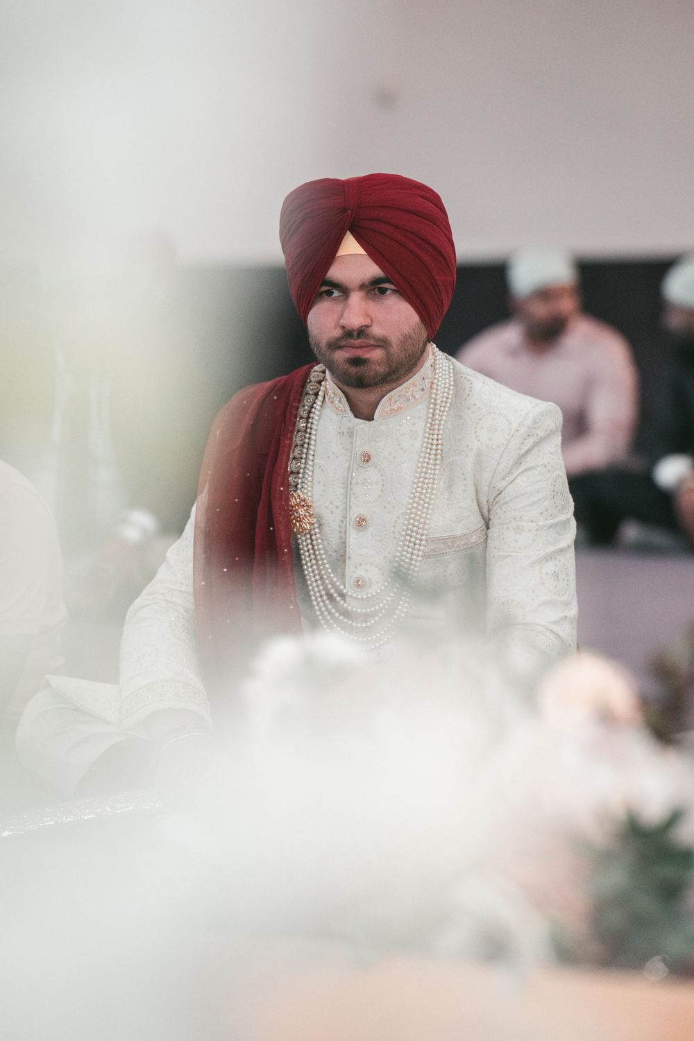 Traditional Sikh groom wearing white sherwani and maroon turban.