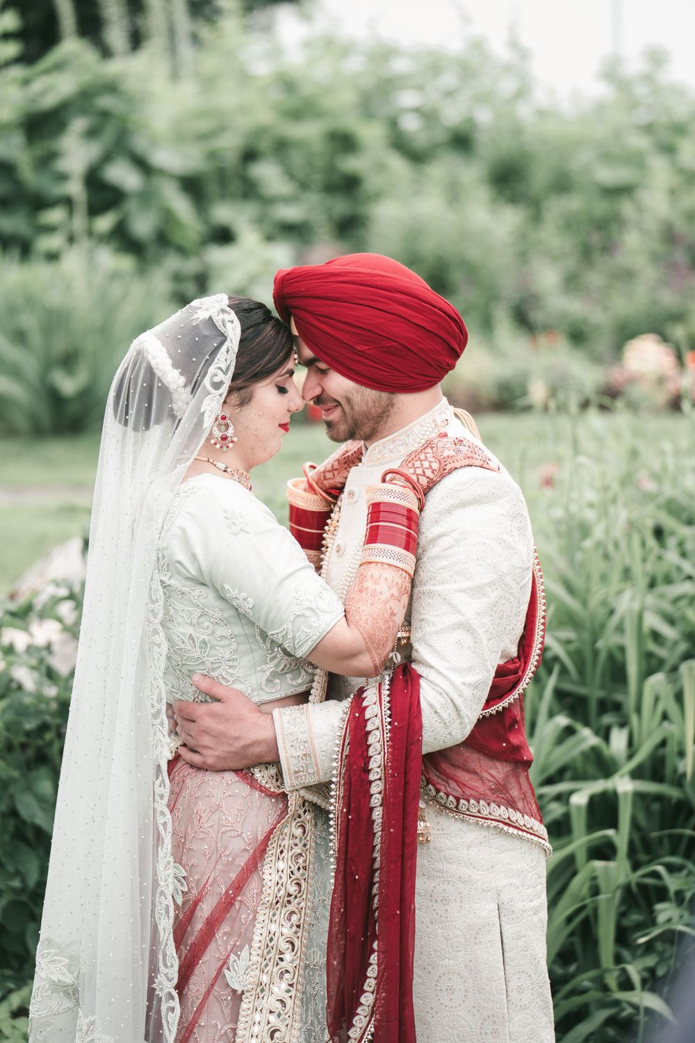 Intimate moment between newlyweds in traditional Sikh wedding attire in garden setting.