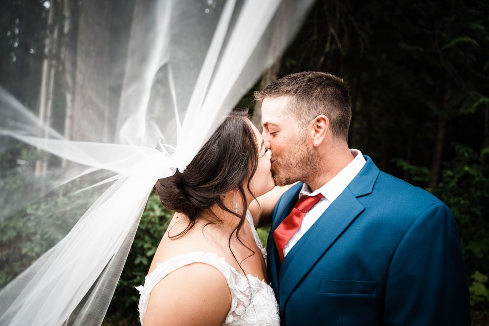A romantic wedding moment captured with flowing veil and evergreen forest backdrop.