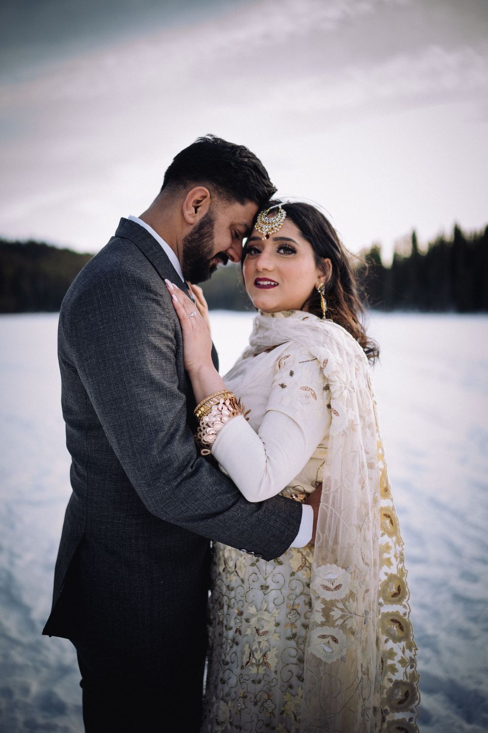 A winter wedding portrait featuring traditional South Asian bridal attire against a snowy landscape.
