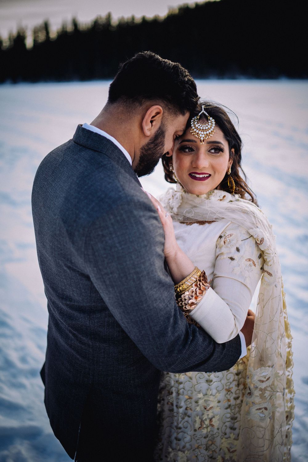 Intimate wedding portrait with traditional South Asian bridal jewelry and attire by a frozen lake.