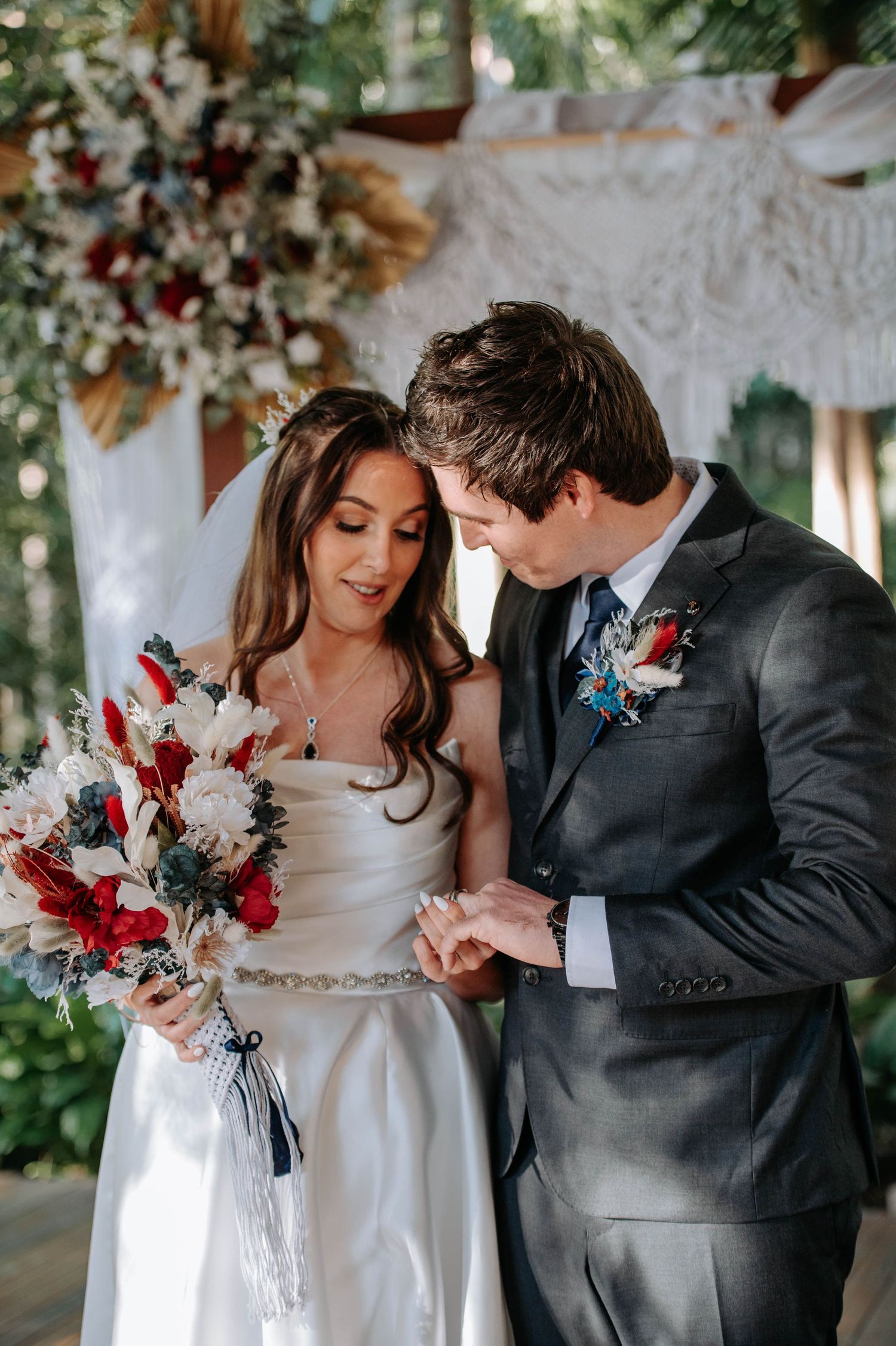Intimate wedding portrait features elegant bouquet with red and white flowers amid floral decorations.