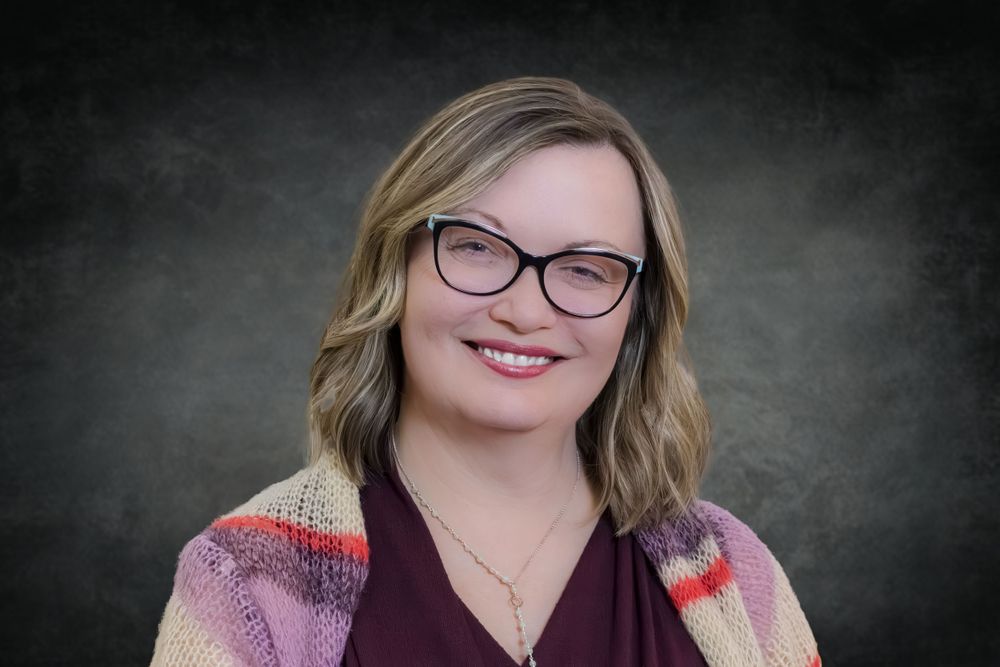 Professional headshot against dark background showing warm smile and glasses.