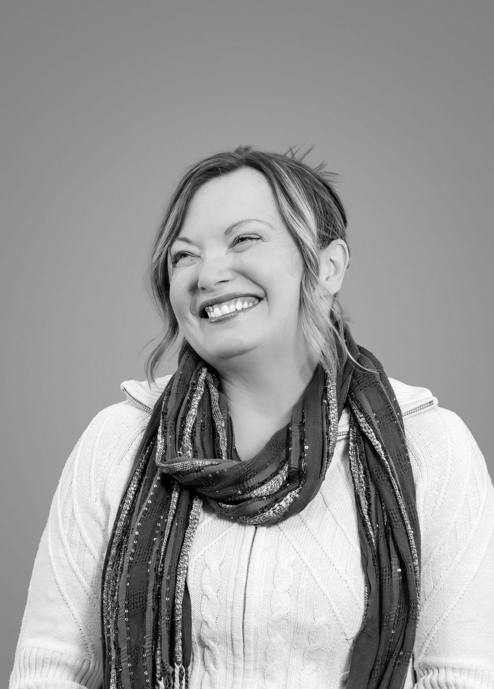 Black and white portrait of laughing person wearing patterned scarf.