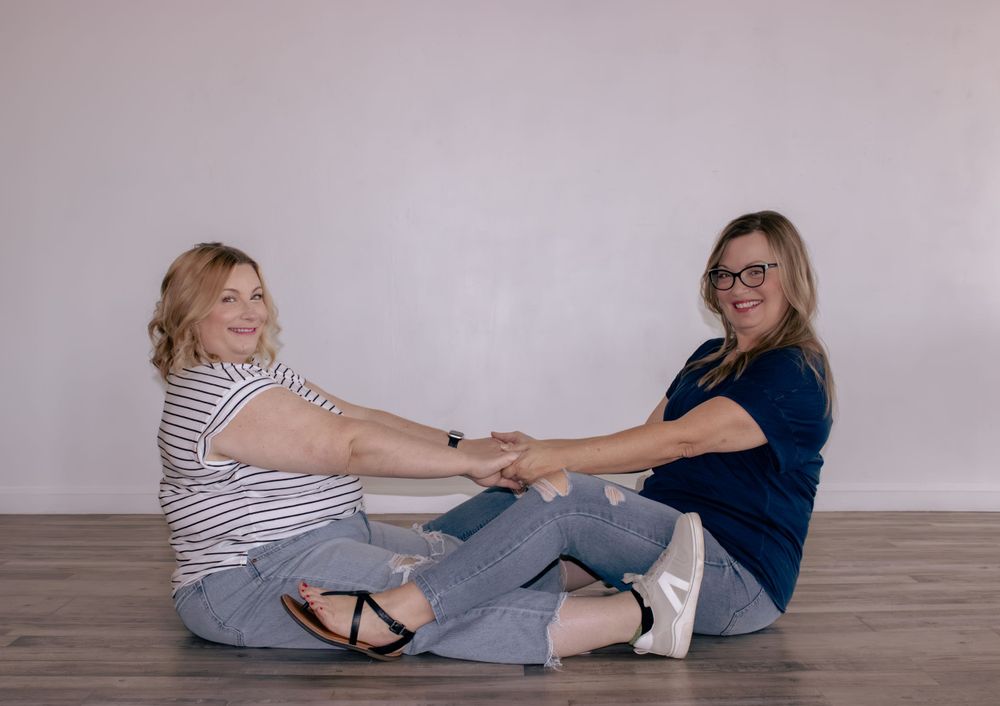 Two people sitting on wooden floor playfully holding hands and smiling.