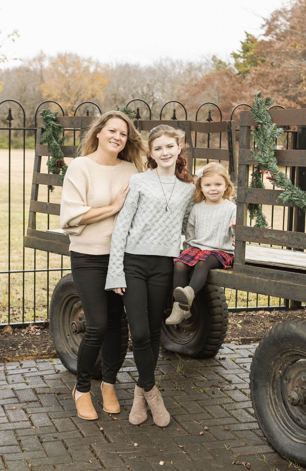 Three people pose together on a rustic wagon during autumn.