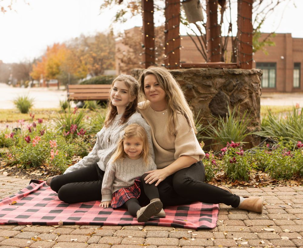 Outdoor autumn family portrait on a plaid blanket near decorative stone pillars.