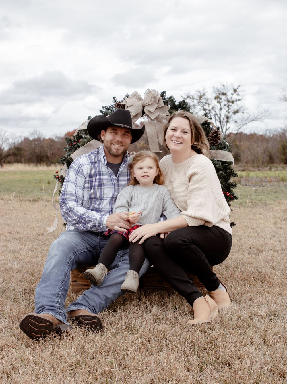 Family portrait in countryside setting with rustic wreath backdrop in a field of dried grass.