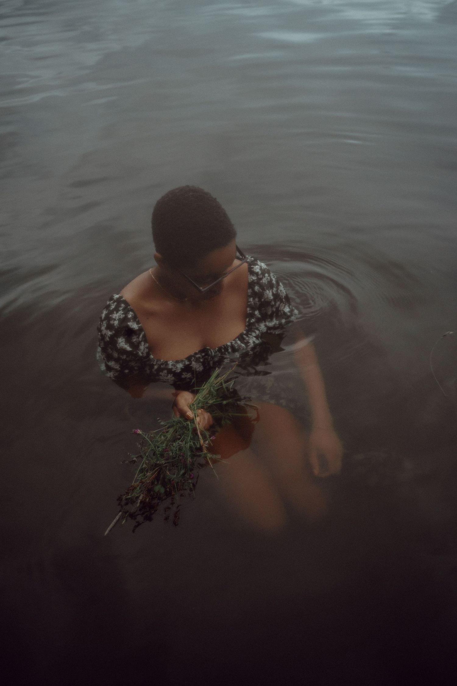 Person in floral dress holds plants while standing in dark water.