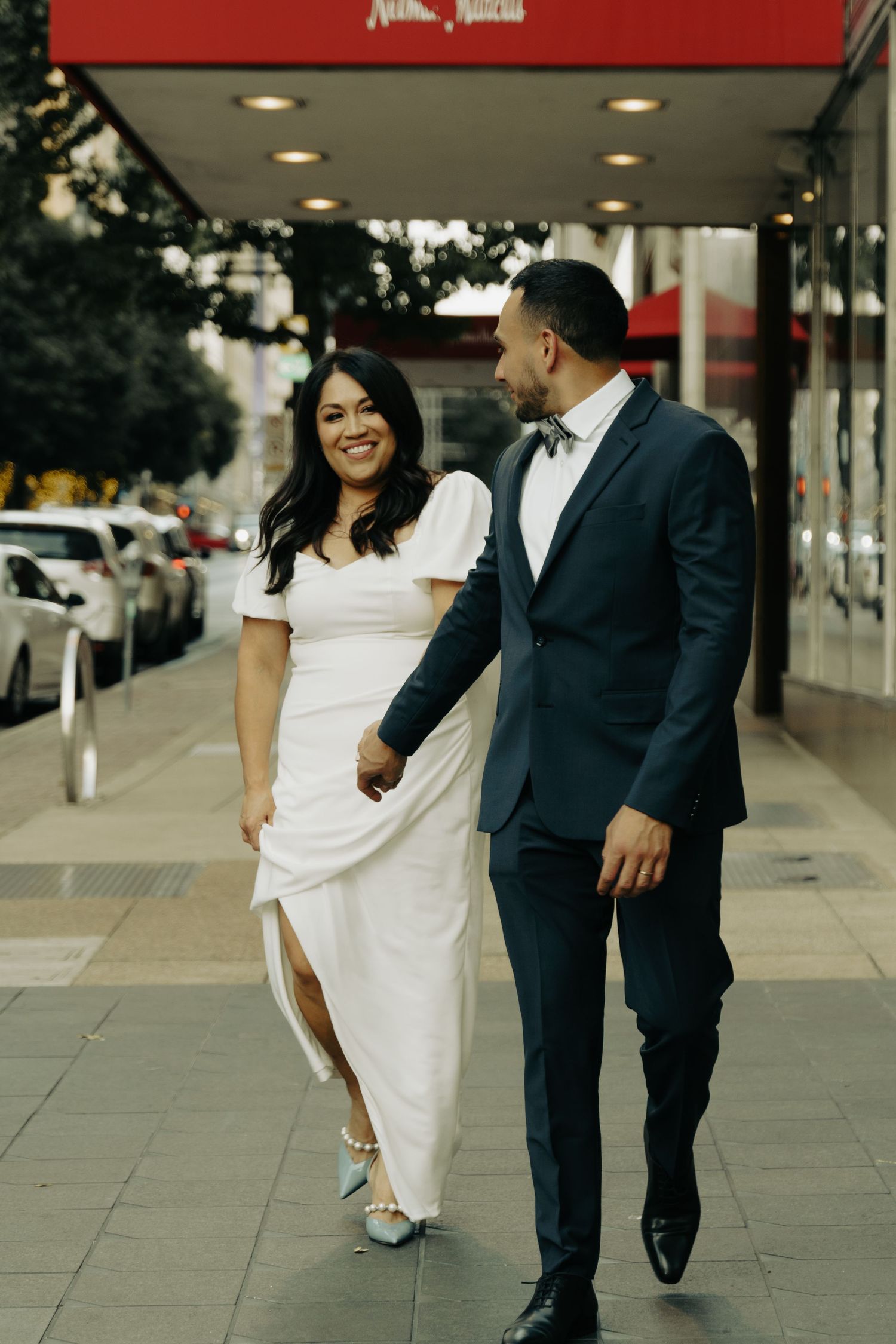 A couple walking and smiling together outside a storefront with red awning.