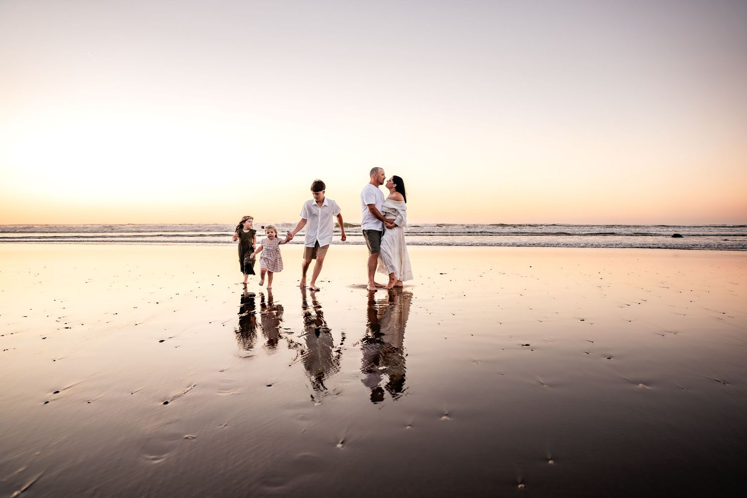 A family enjoys quality time together on a reflective beach at sunset.