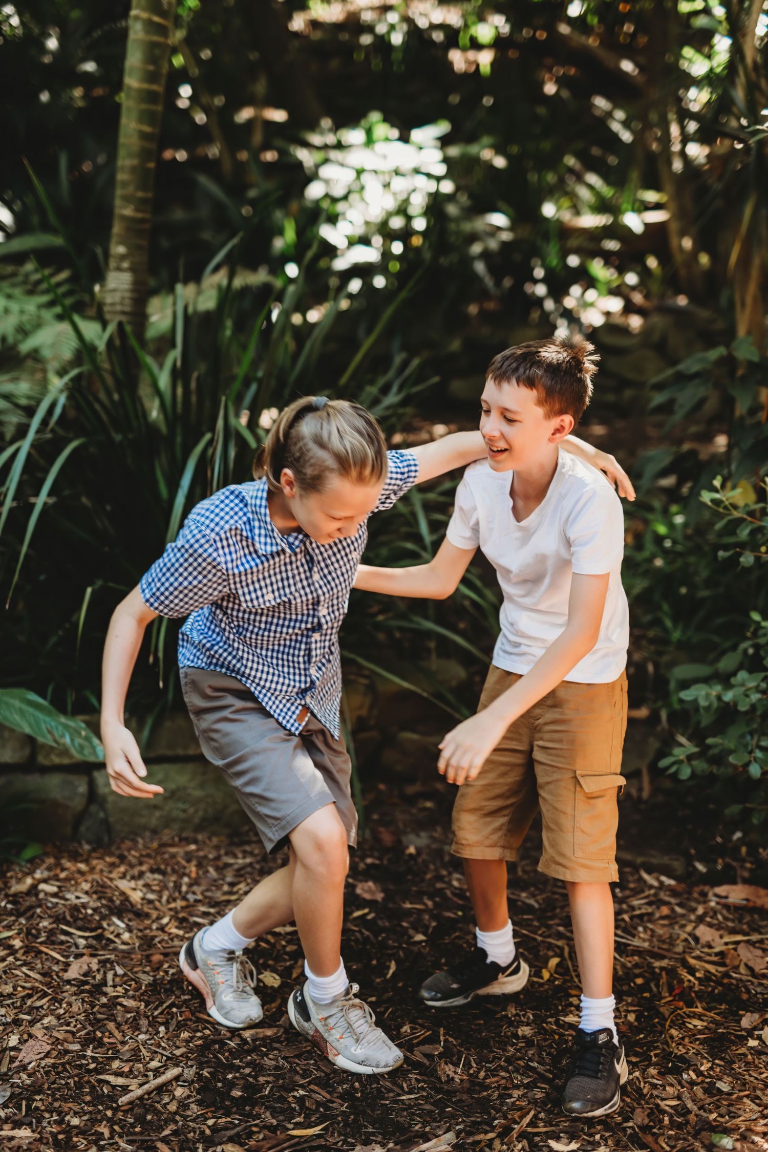 Two playful kids horsing around on a forest trail covered with wood chips.
