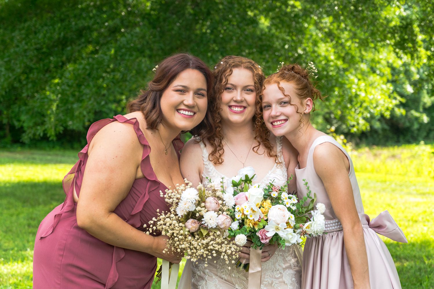 A joyful outdoor wedding photo with bouquets and matching dresses.
