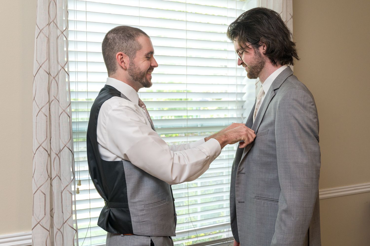 Two people adjusting formal wear and ties before a wedding ceremony.