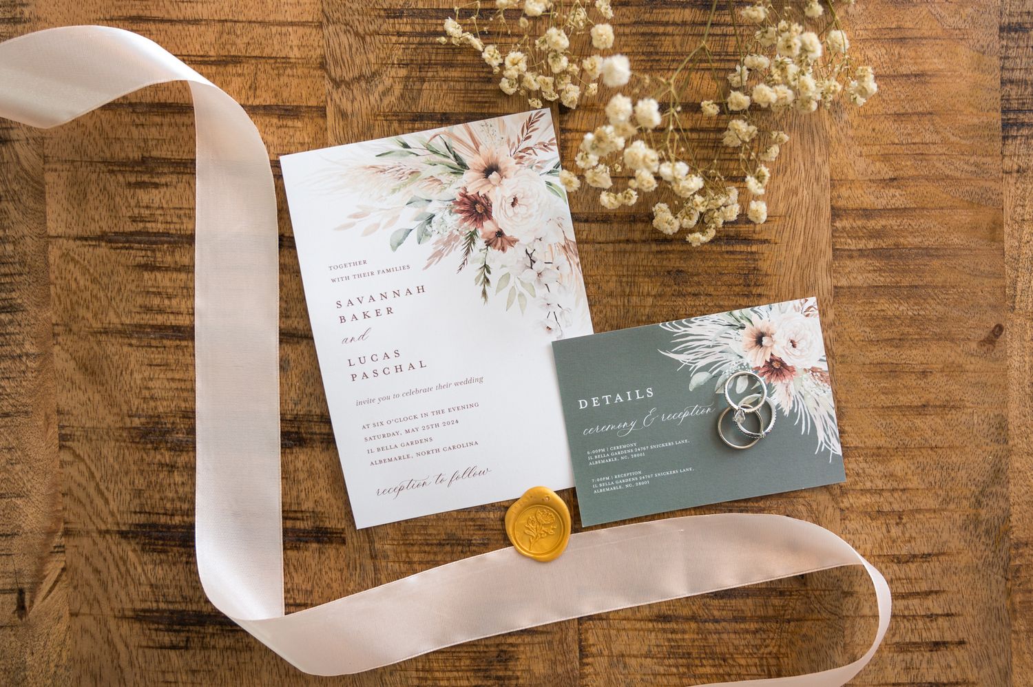 Wedding invitations with floral design and white ribbon on rustic wooden background.