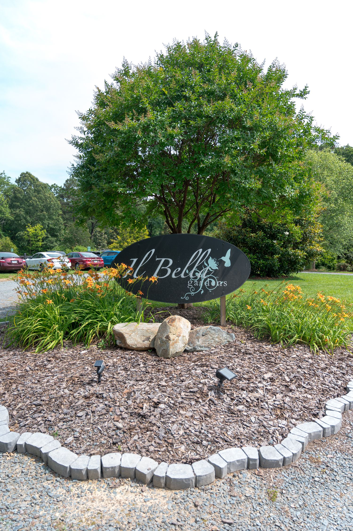 A landscaped entrance sign for 'The Bella' with a large shade tree and decorative stone border.
