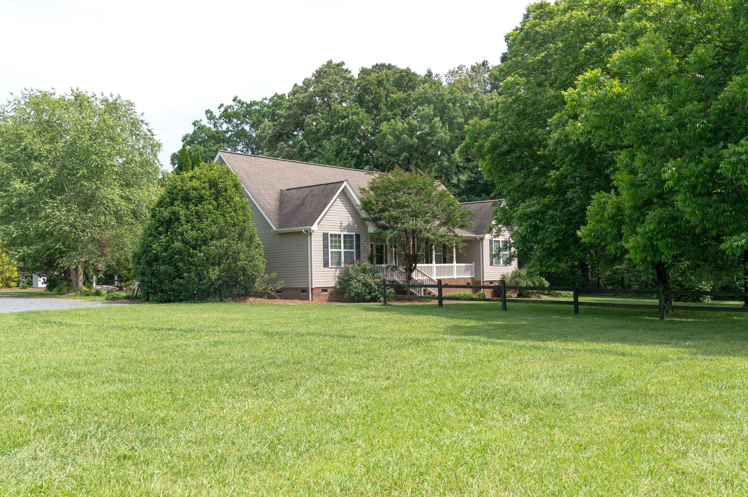 Grey house with white trim situated on spacious green lawn surrounded by mature trees.