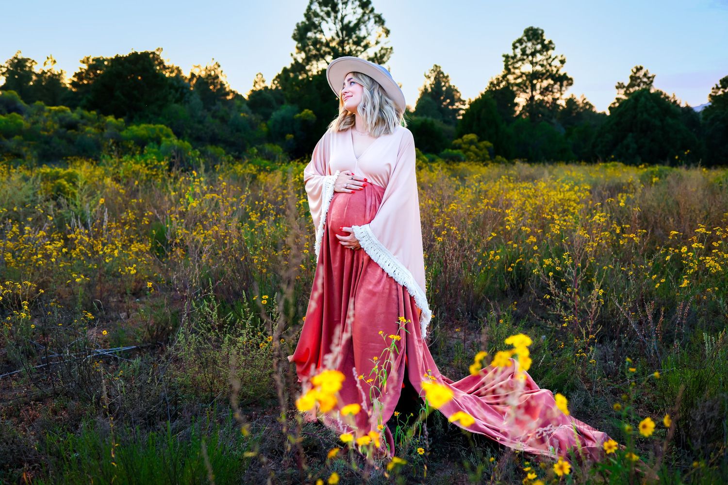 Ethereal maternity portrait in a flowing red dress amidst wildflowers at sunset.
