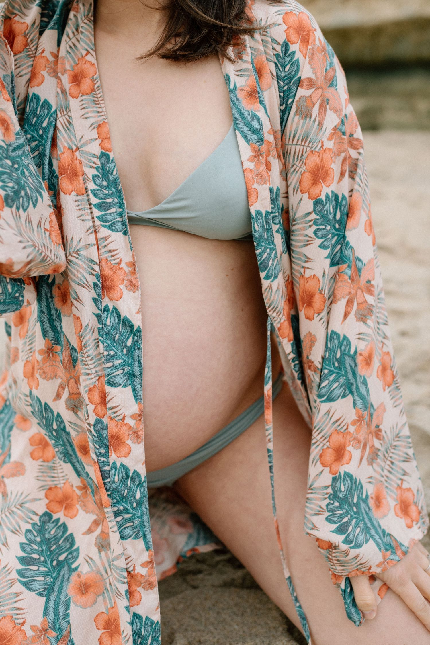 A floral kimono robe with teal and coral patterns covering a pregnant belly in swimwear during maternity photoshoot in San Diego.
