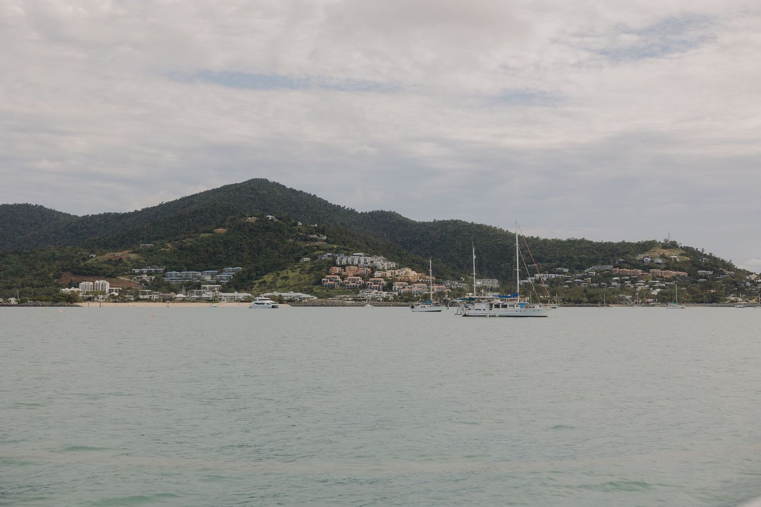 Coastal town nestled on hillside with boats in harbor under cloudy skies.