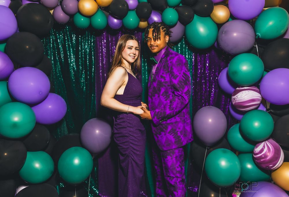 A celebratory party scene with teal and purple balloons against a dark backdrop decorated with sparkly tinsel curtains.