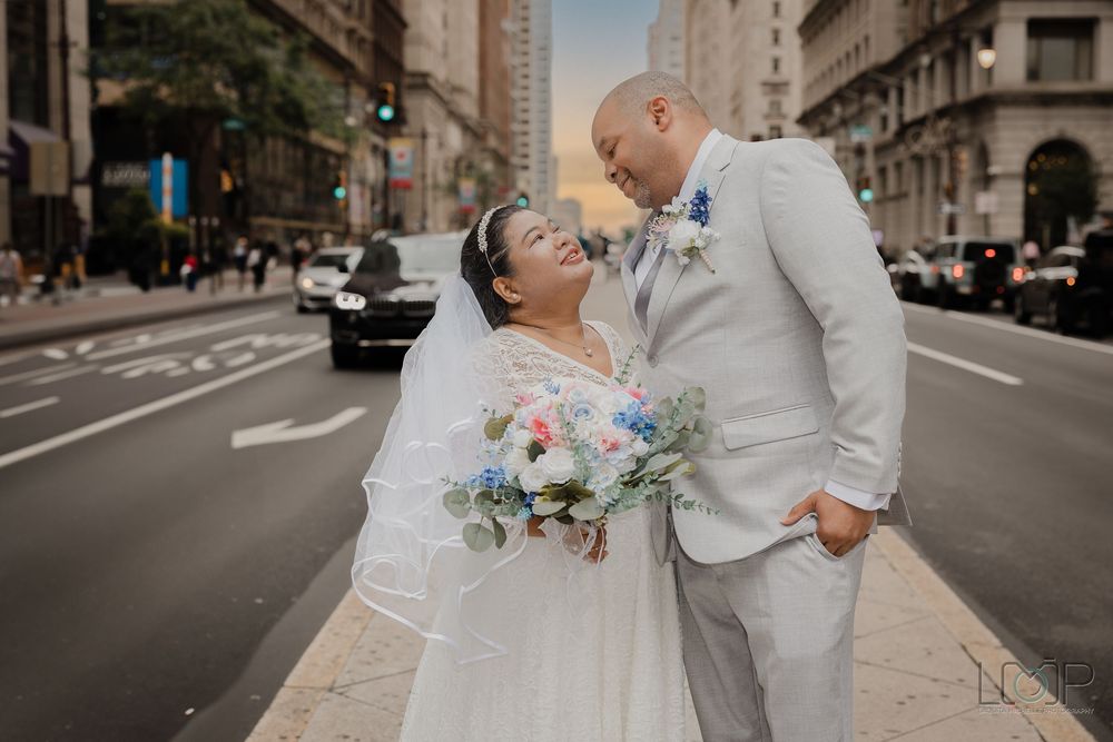 A wedding couple embraces on an urban street lined with historic buildings while holding a bouquet of flowers.