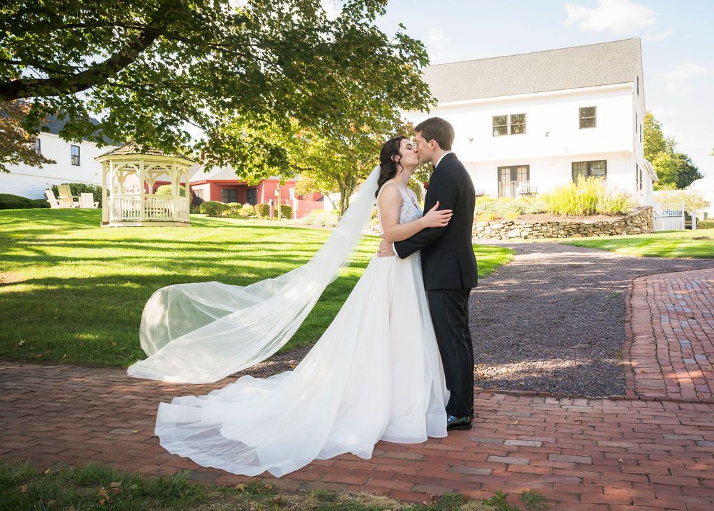 A flowing white wedding dress billows dramatically in the breeze on a brick pathway during a sunset photoshoot.