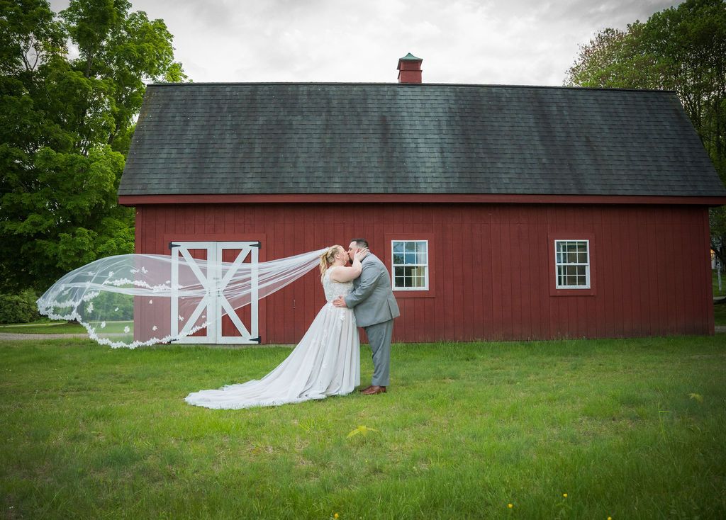 A panoramic view of a rustic red barn and green lawn set against an overcast sky during a wedding celebration.